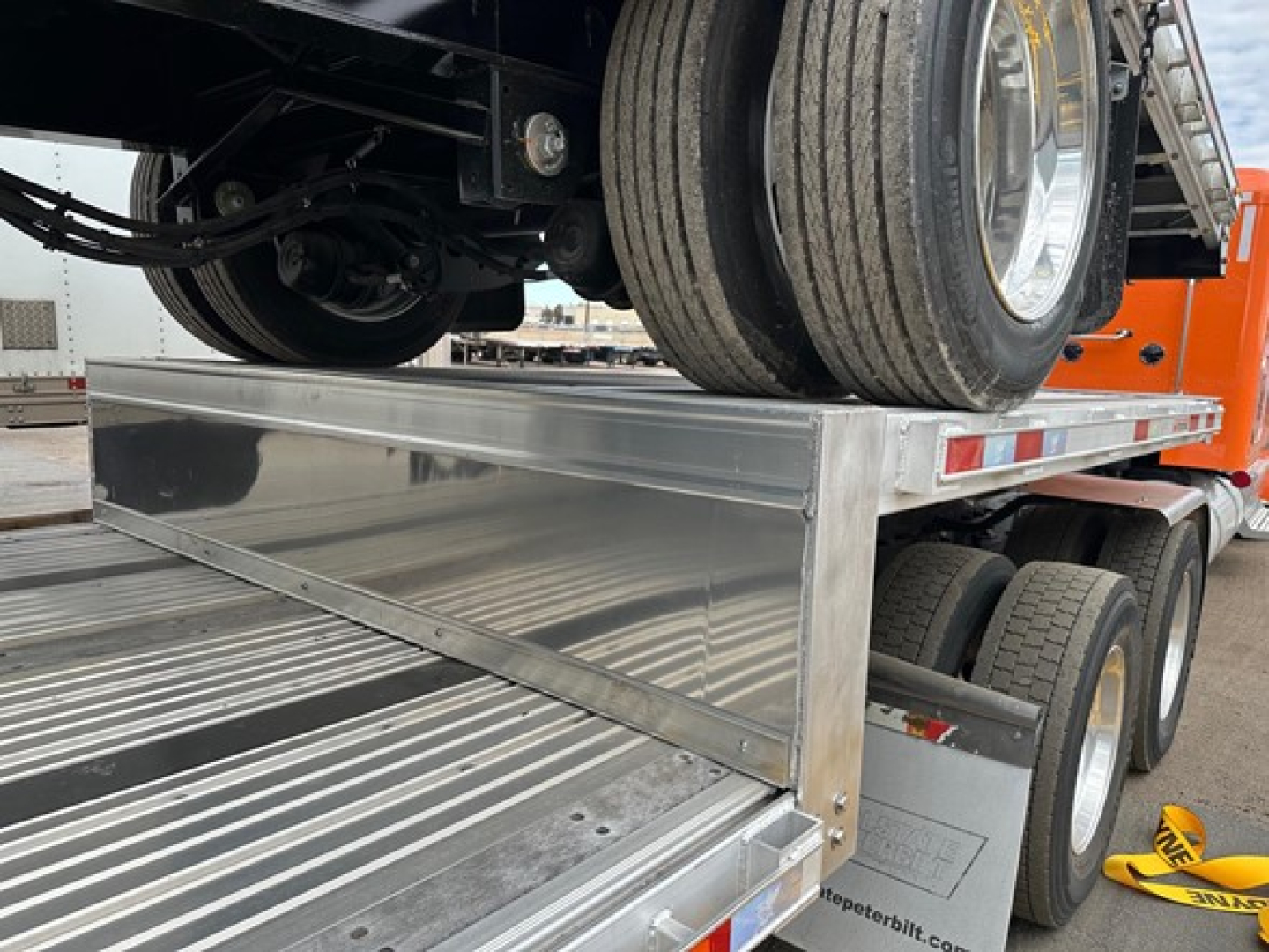 Manac combo drop deck trailer with dual rear axles and aluminum deck, rear view showing vertical drop tail and spare tires.