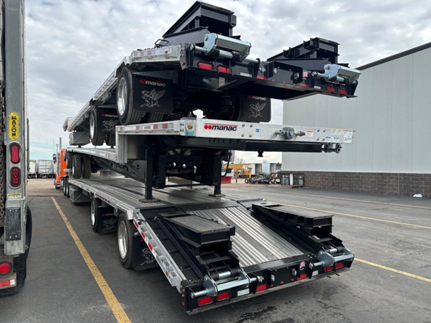 Manac combo drop deck trailer loaded on flatbed with two carousels at rear, reflective tape, and multiple axles; VIN 150118973247 visible on trailer.