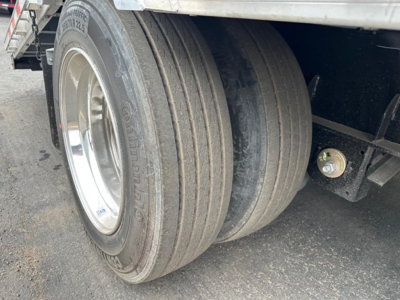 Truck trailer dual rear tires with metal wheel rims and black undercarriage; partial white side panel above; visible decal on tire sidewall reading 'Goodyear' and other faint markings.