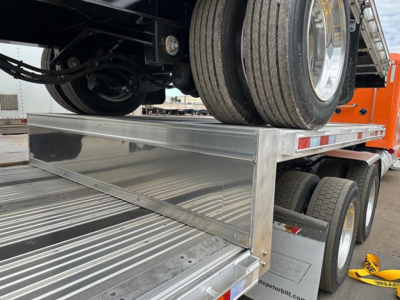 Trailer deck edge with aluminum drop deck and dual rear axles; visible tires and chrome decking.