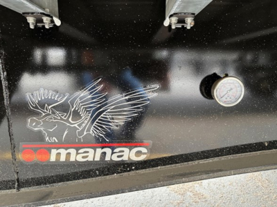 Manac trailer back panel showing logo and pressure gauge with black finish and white bird emblem.
