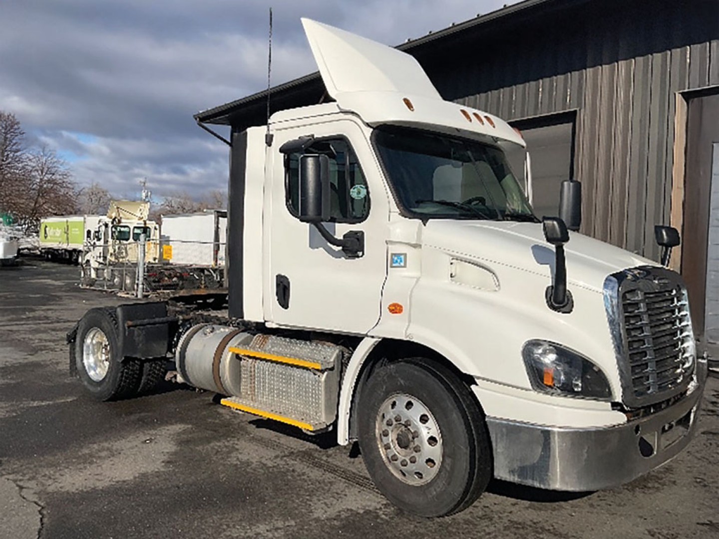 Freightliner Cascadia113 tractor cab side view showing front grille, fuel tanks, and missing trailer with stock number sticker.