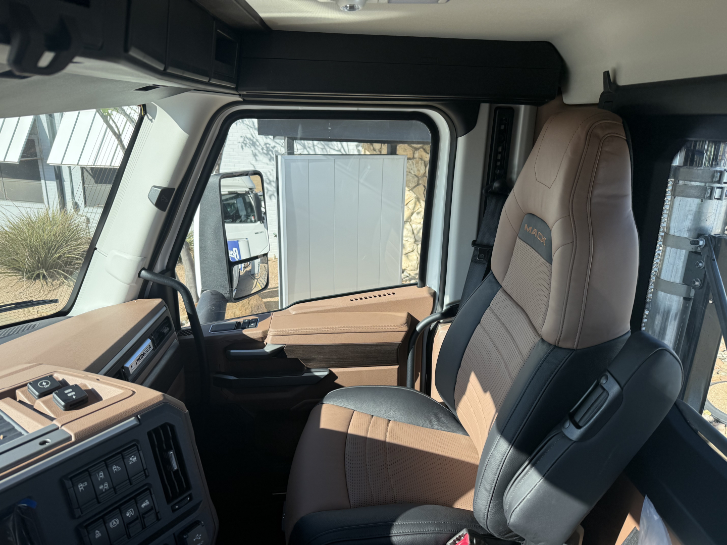 Interior of 2026 Mack PR64T cab showing brown and black leather seat, control panel with switches, and window framing.
