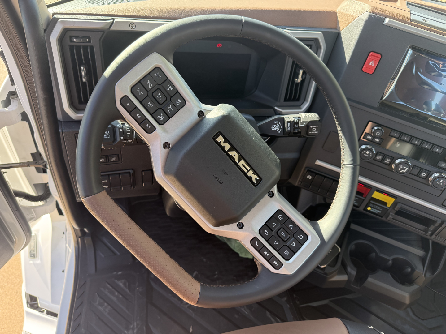 Mack PR64T truck interior showing steering wheel with mounted controls and dashboard displays.