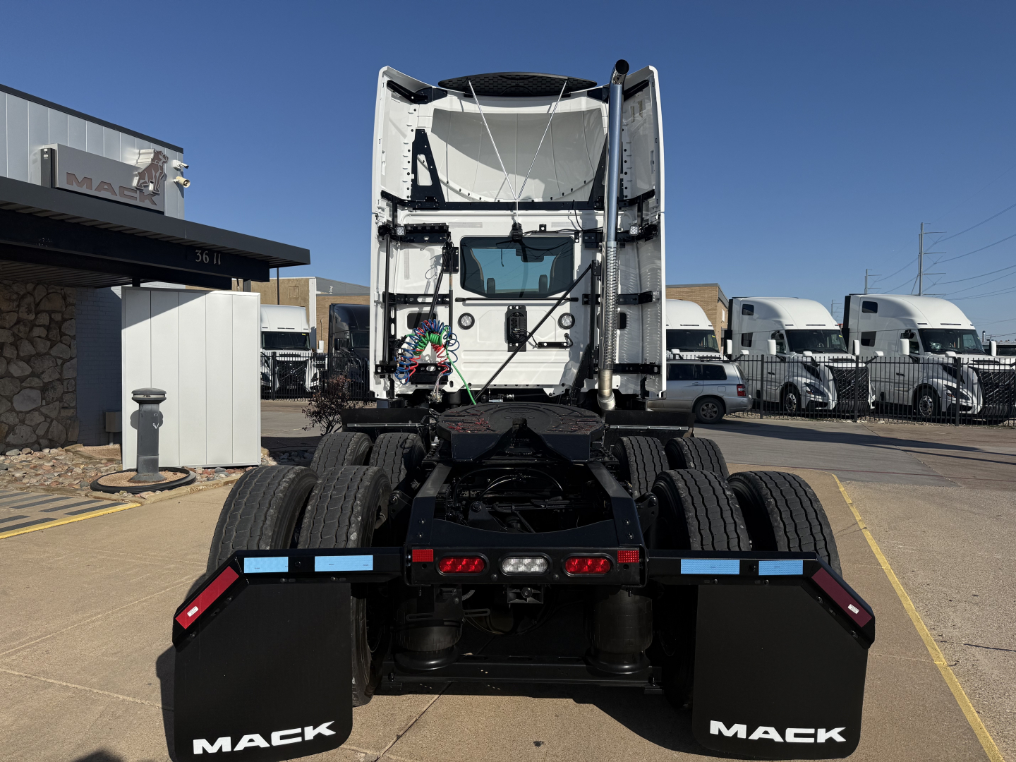 Mack PR64T tractor rear view showing dual rear axles, fifth wheel, and rear fenders with Mack branding. Available text visible on the vehicle includes 'MACK' on mud flaps and the general rear view of a new conventional daycab tractor.