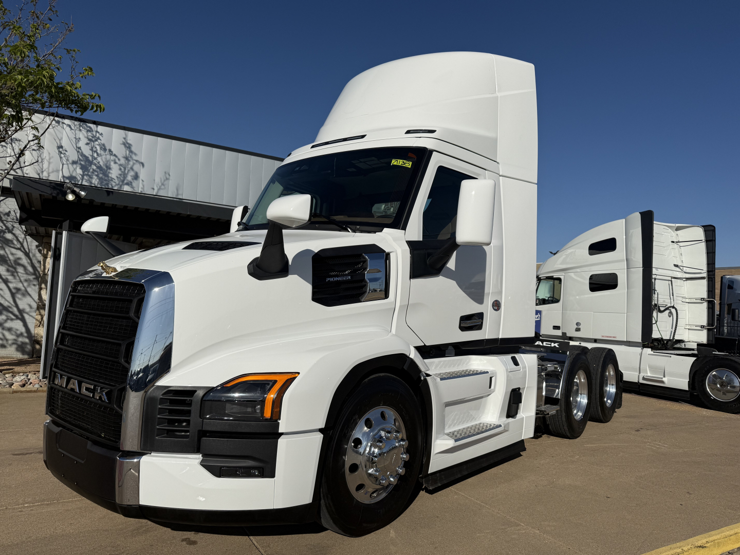 Truck cab and sleeper daycab tractor showing Mack emblem on black grille, headlights, white exterior, chrome wheels, fuel tanks, and side steps.