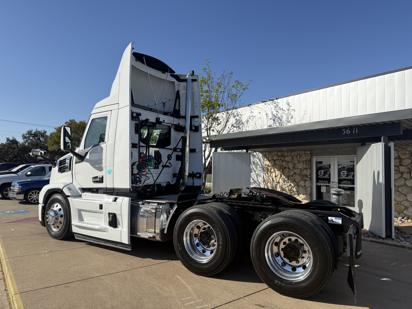 Mack PR64T conventional daycab tractor shown from left rear side with open cab, dual rear axles, chrome fuel tanks, and wheel rims.