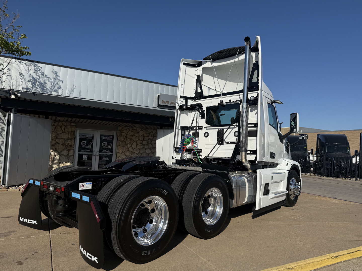 Mack PR64T heavy duty truck with white cab, dual rear axles, and exposed engine bay area; visible components include rear wheels, fifth wheel, and mud flaps labeled 'MACK'.
