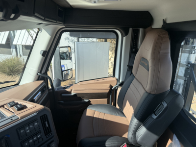 Interior of 2026 Mack PR64T cab showing brown and black leather seat, control panel with switches, and window framing.