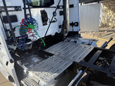 Mack PR64T truck cab interior showing metal step deck and coiled air lines near rear of driver seat area.