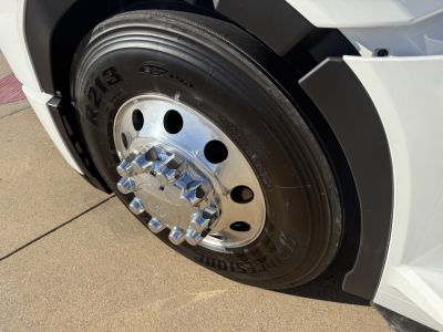 Mack PR64T truck front wheel with polished hub and lug nuts, tire branding visible, white fender and body panel nearby.