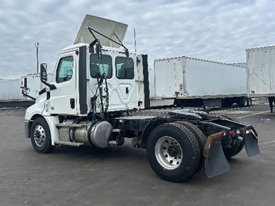 Heavy-duty Freightliner Cascadia daycab chassis with a raised hood and dual rear axles; white cab with fuel tank, side steps, and prominent exhaust; no cargo in trailer areas visible.