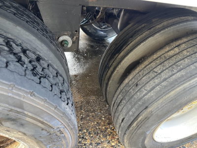 Trailer axle area with two dual tires, wet ground, undercarriage visible, rear wheel area