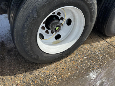 Wheel hub area of a 2023 Hyundai trailer with a white steel rim and black tire, showing lug nut holes and hub center.