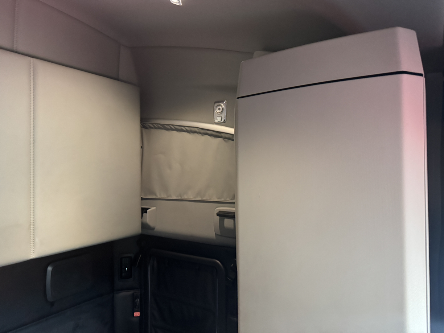 Kenworth T680 cab interior showing sleeper area with light gray panels and a vertical storage unit.