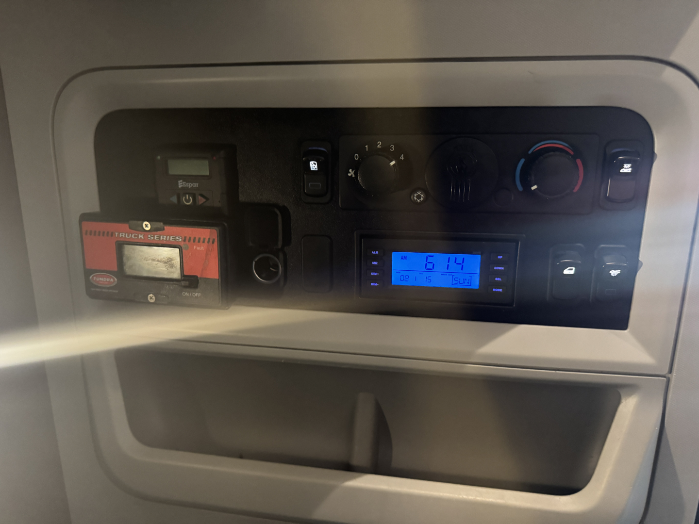 Kenworth T680 interior dash panel showing radio/display unit and climate controls, with a small red device slot to the left and a blue digital display reading 6:14.
