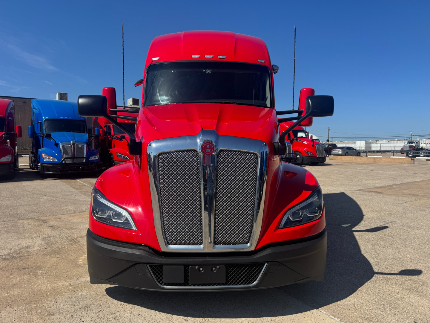 Kenworth T680 front view showing large chrome grille, red hood, black bumper, and side mirrors.