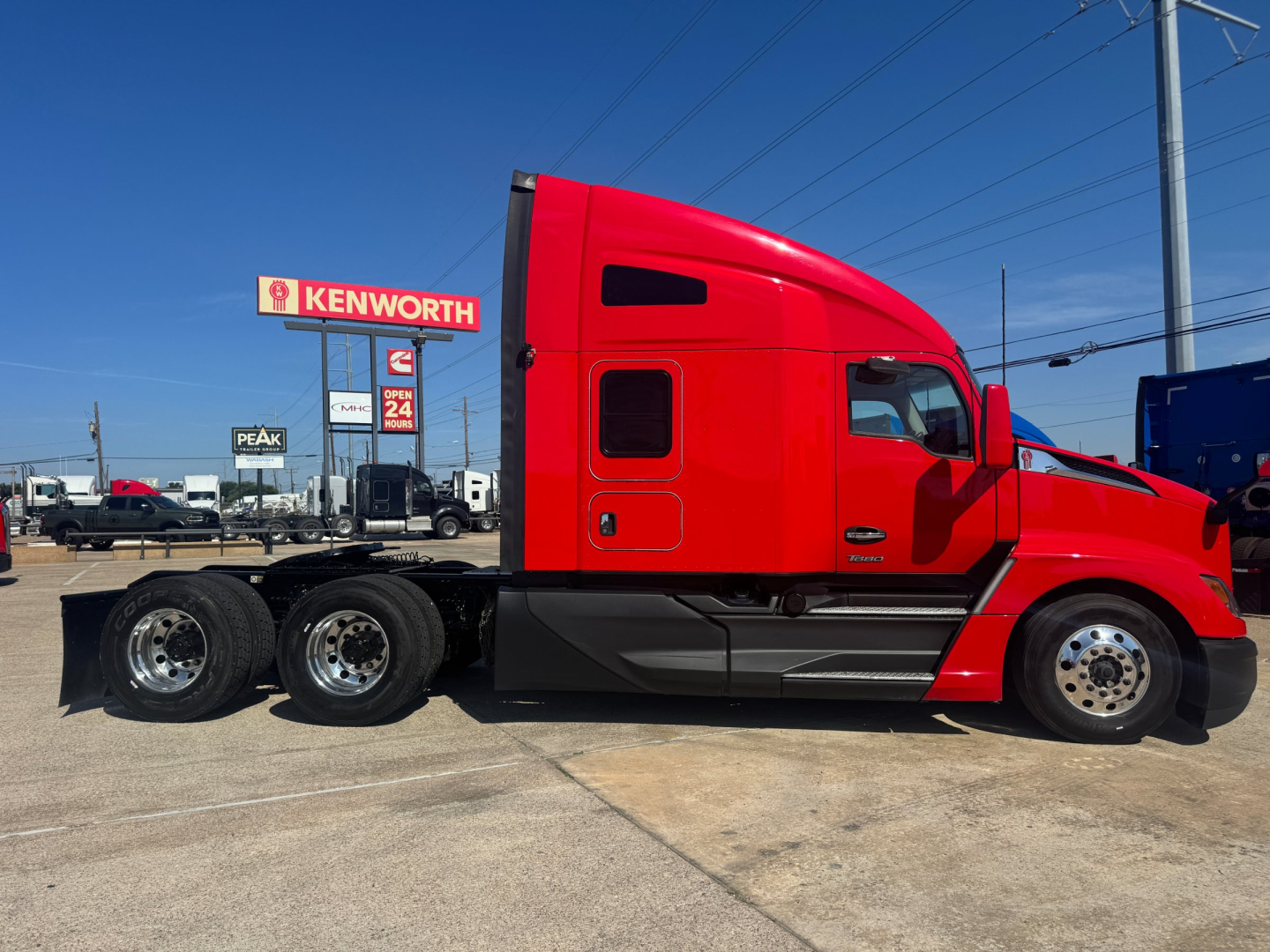 Kenworth T680 tractor trailer in red color side view showing sleeper cab and 3 rear axles, dealership lot in background.