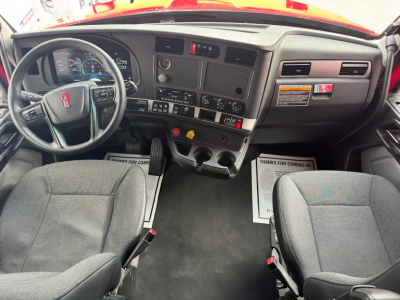 Kenworth T680 cab interior showing steering wheel with Kenworth emblem, center dashboard with gauges, control switches, and two front seats.