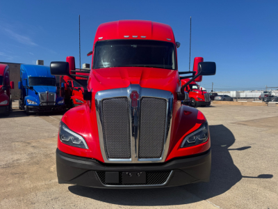 Kenworth T680 front view showing large chrome grille, red hood, black bumper, and side mirrors.