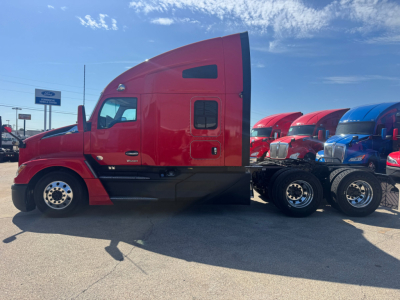 Kenworth T680 sleeper cab tractor side view showing red truck with black chassis and spare wheels in background.