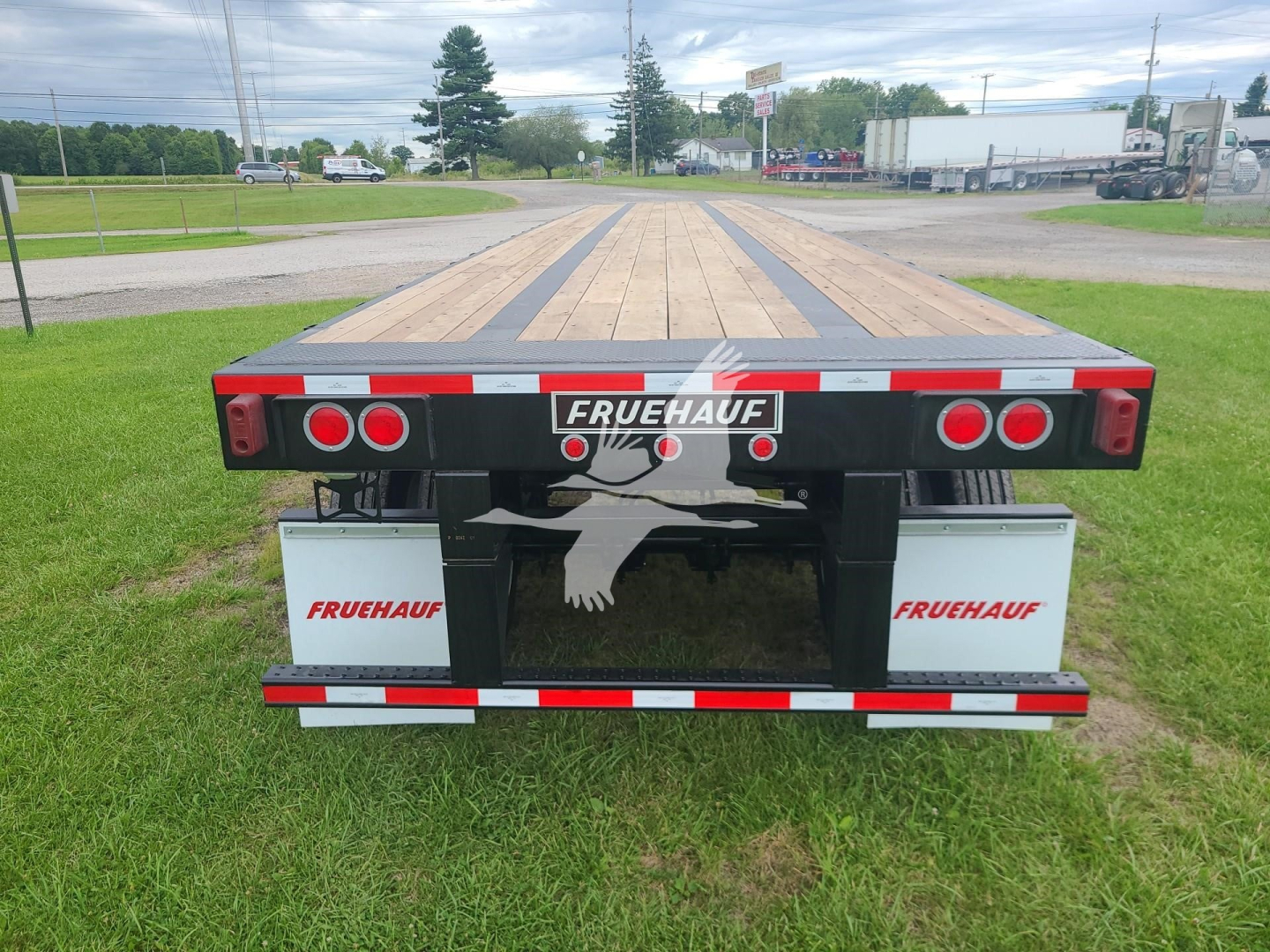 Fruehauf flatbed trailer rear view showing tail lights, bumper, and Feber logo; wooden planks on deck; Fruehauf branding on mudguards and rear center.