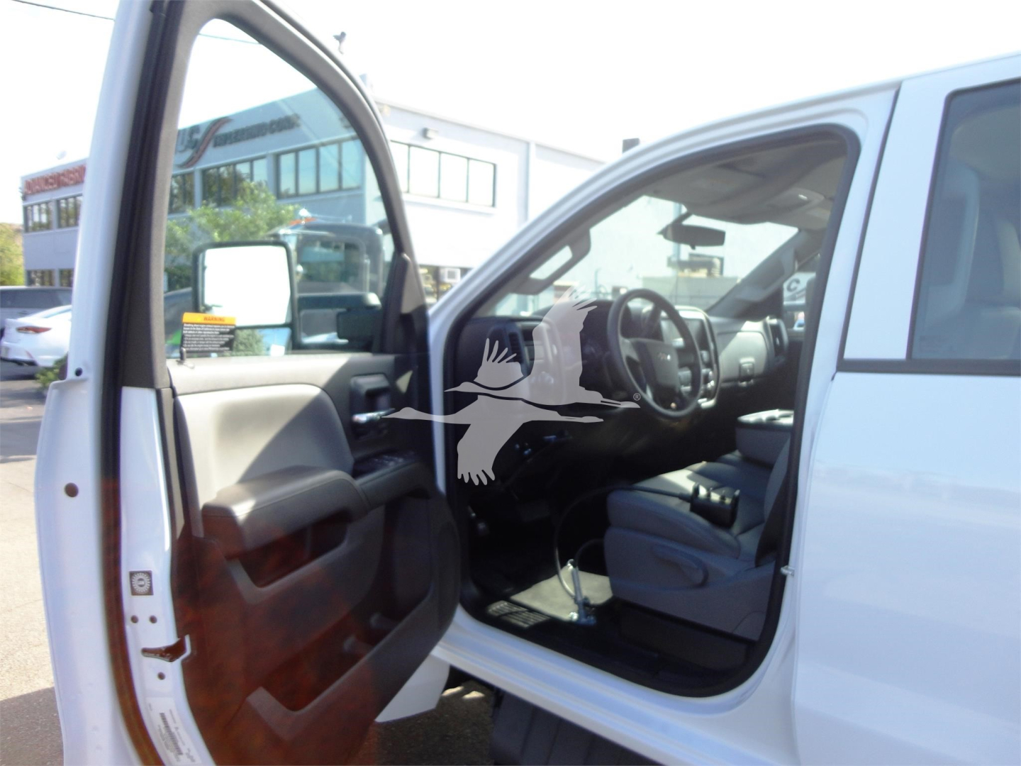 Interior of a white Chevrolet Silverado 5500HD cab with the driver door open, showing steering wheel and front seat.