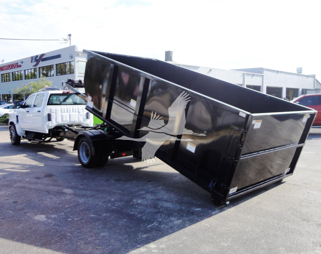 Truck with dark dump bed tilted on a white tow truck in a parking lot. Side graphic shows white hands lifting. No legible model text visible.