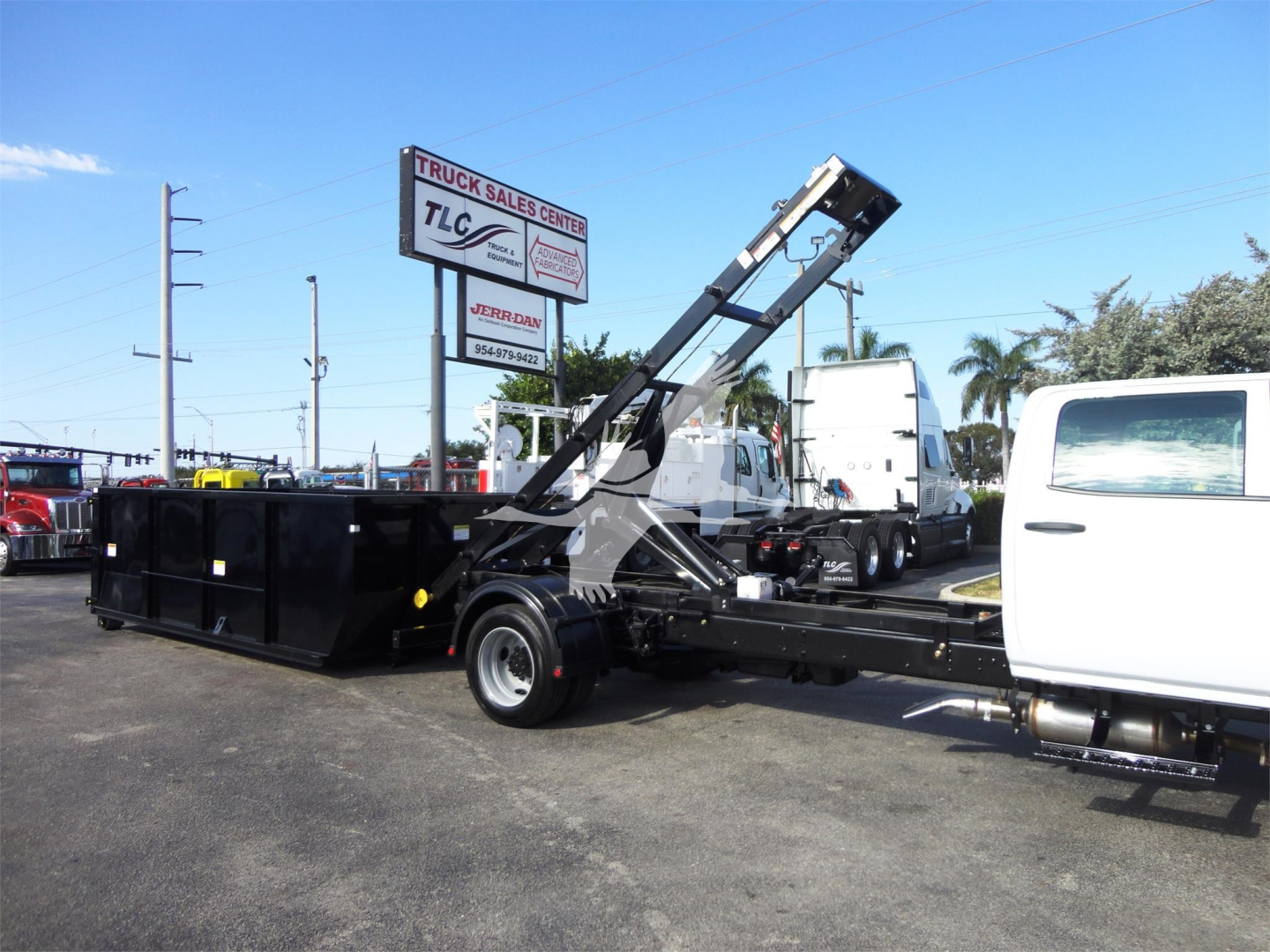 Truck-mounted roll-off truck with white cab and blackable hydraulic lifting arm, loading container in an outdoor lot