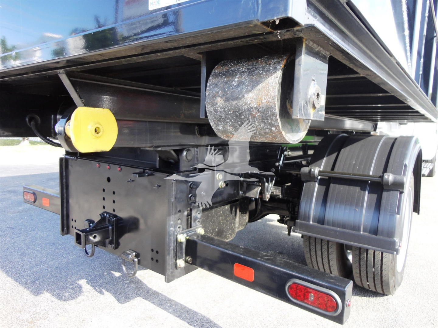 Rear underside of a 2023 Chevrolet Silverado 5500HD roll-off truck showing hitch assembly, yellow parking brake knob, toolbox, and wheel with fender.