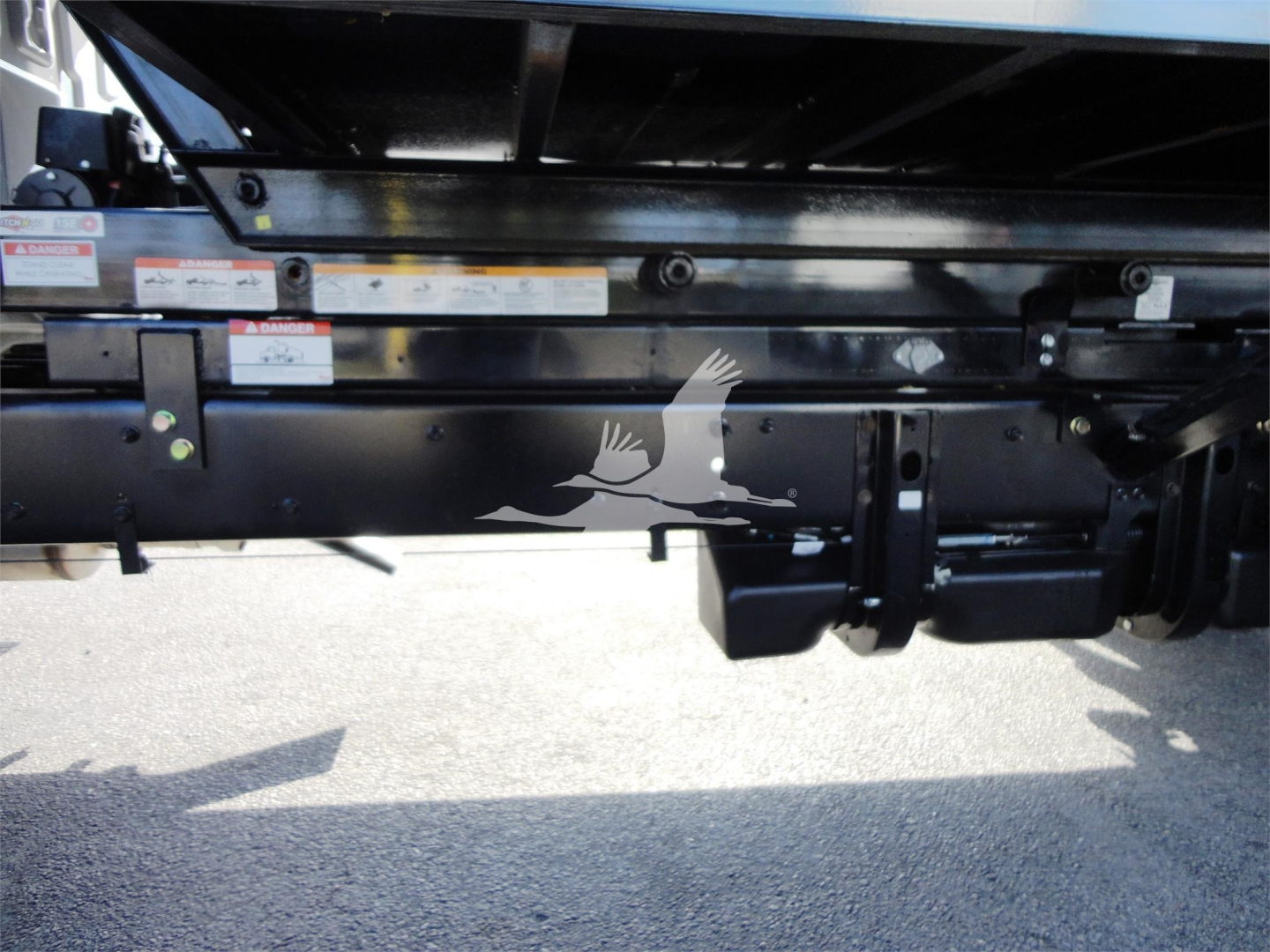Truck chassis underside showing hitch and frame rails with warning labels and metal components.
