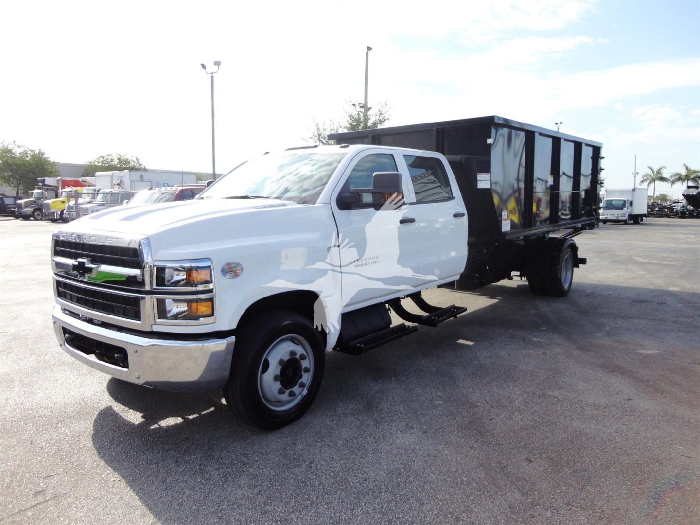 Chevrolet Silverado 5500HD dump body truck side view showing white cab and black dump bed trailer at a truck lot.
