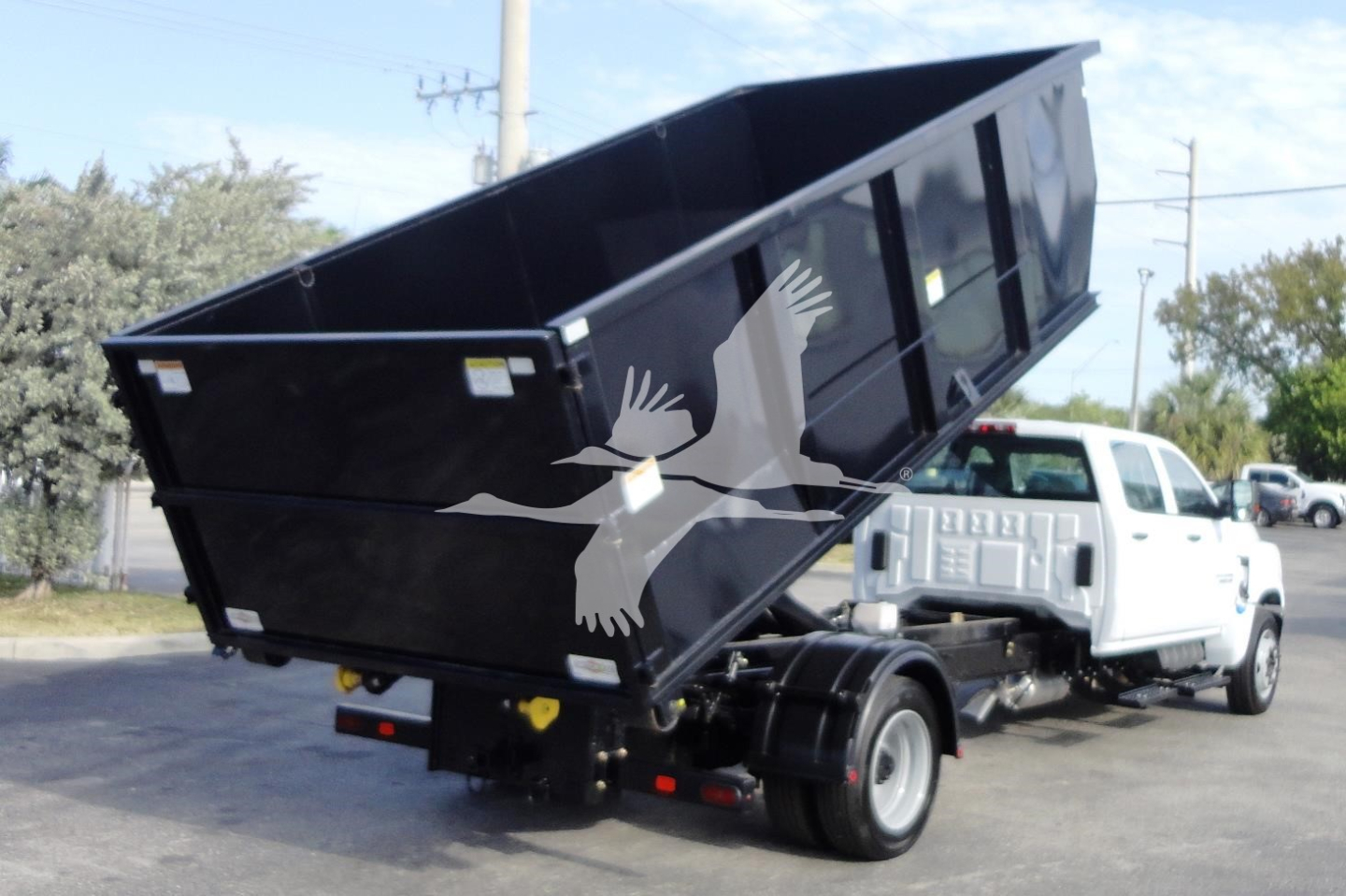 Chevrolet Silverado 5500HD dump truck in roll-off configuration with black bed raised to dump position; white cab visible; no legible text on components.
