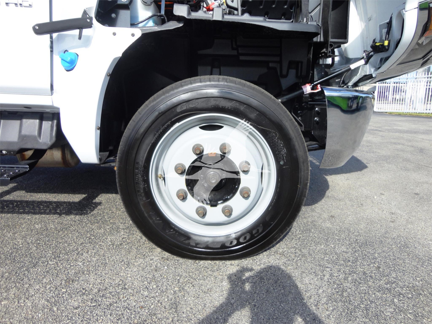 Wheel and front suspension area of a 2023 Chevrolet Silverado 5500HD rolloff truck showing steel alloy wheel with lug nuts and tire, part of front wheel well and cab components.