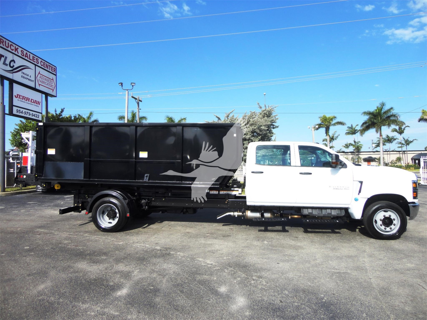 Chevrolet Silverado 5500HD rolloff truck side view showing black dump body with white cab and logo bird graphic.