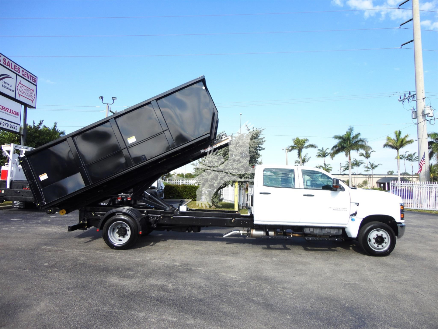 Truck showing a white 2023 Chevrolet Silverado 5500HD roll-off with a raised dumping hopper in a dealership lot