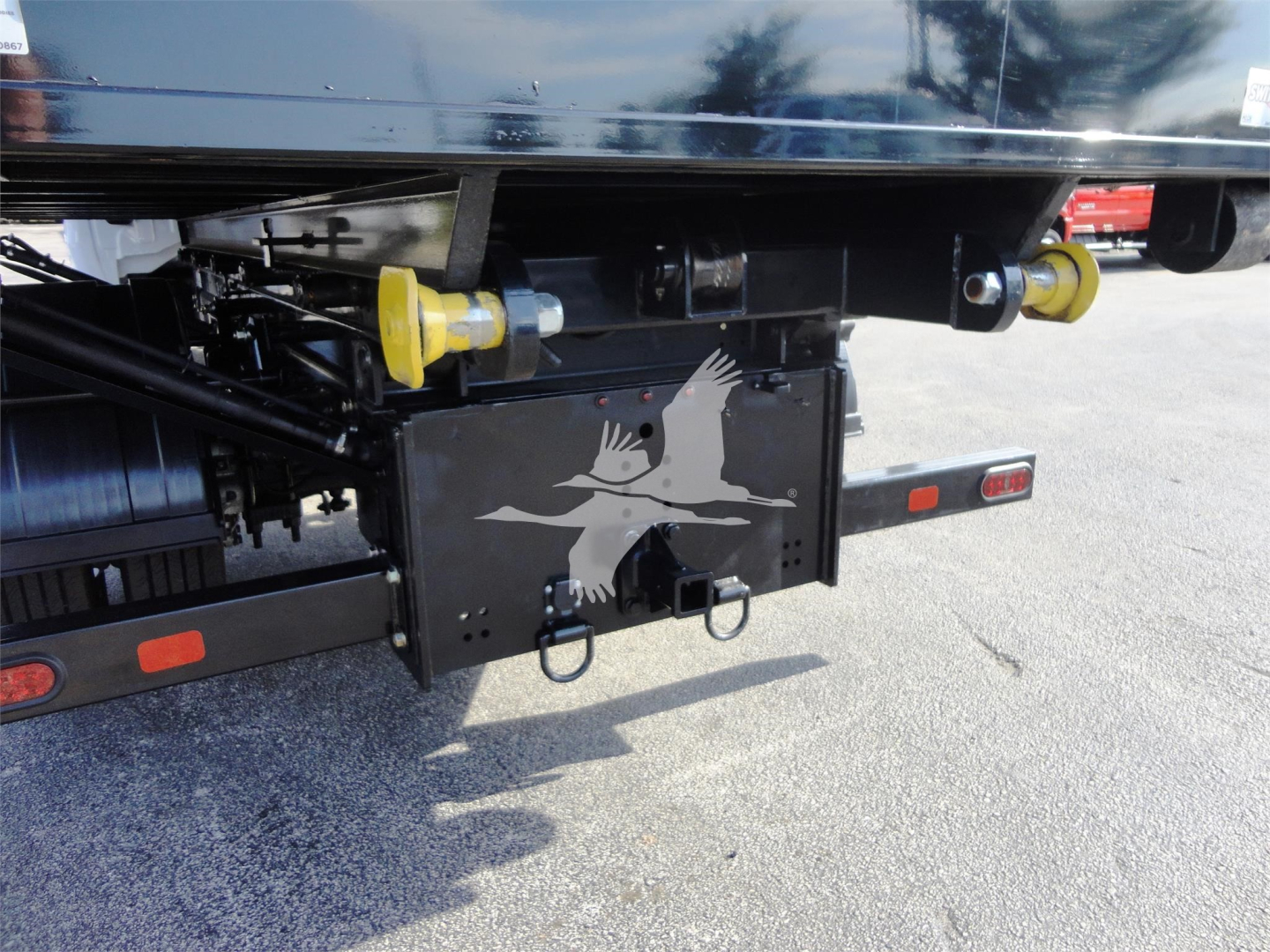 Rear view of 2023 Chevrolet Silverado 5500HD rolloff truck showing rear bumper, yellow towing pins, and a black tail device with a white bird graphic.