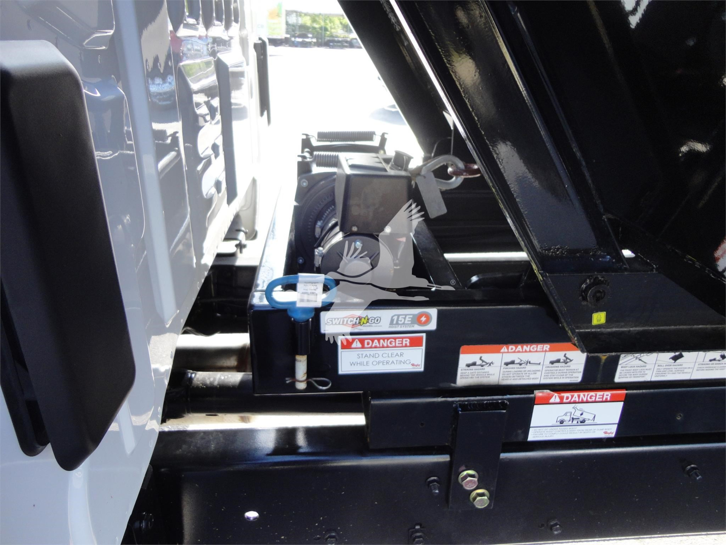 Truck hitch area with hydraulic lift mechanism and warning labels on a Silverado 5500HD truck.