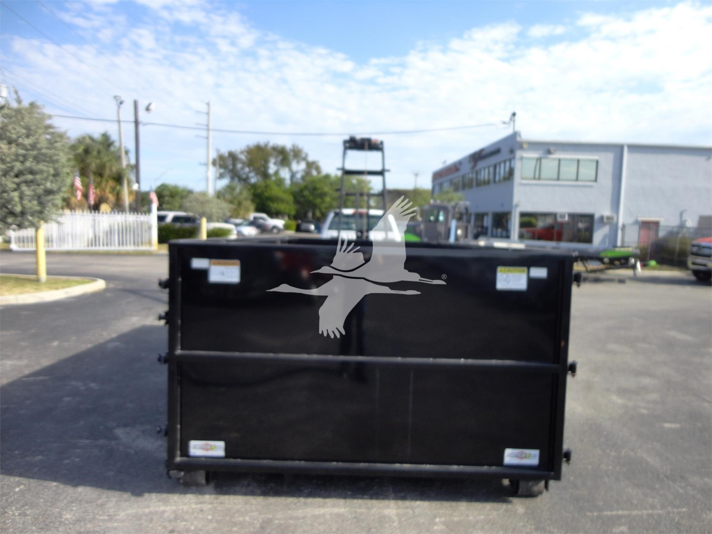 Rolloff truck dump bed in front of a dealership with a large duck logo sticker on the black side panel.
