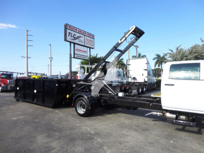 Truck-mounted roll-off truck with white cab and blackable hydraulic lifting arm, loading container in an outdoor lot