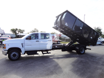2023 Chevrolet Silverado 5500HD chassis with raised dump bed in a tilt position, white cab, black dump body, side view showing unfold mechanism.