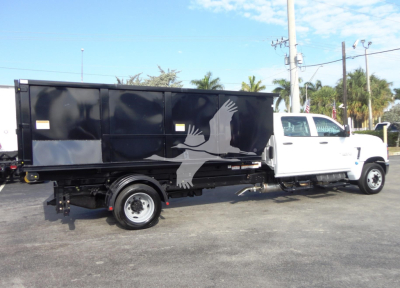 2023 Chevrolet Silverado 5500HD roll-off truck side view showing black cargo enclosure with white pickup cab and crane arm detail.