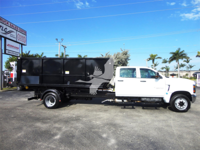 Chevrolet Silverado 5500HD rolloff truck side view showing black dump body with white cab and logo bird graphic.
