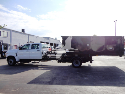 Truck with white cab and black dump body on a sweep bed, side view showing roll-off dumpster truck.