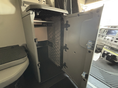Cab interior with an open storage cabinet door showing a vertical small shelf and a shallow upper compartment inside a Volvo VNL truck cabin.
