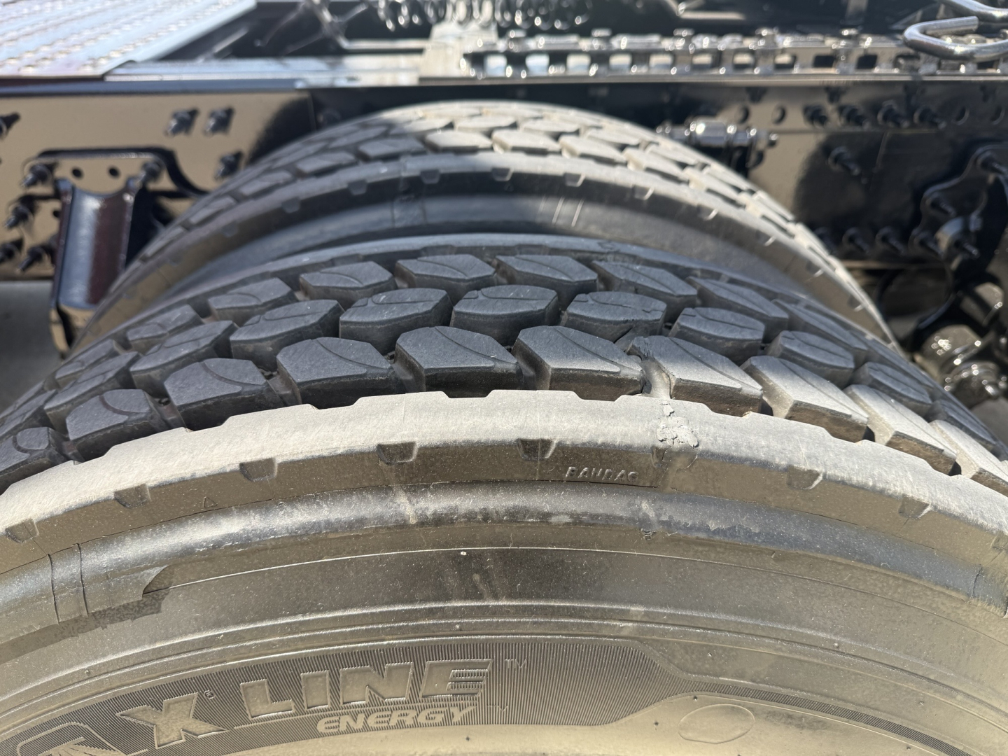 Front left tire and wheel well of a Volvo VNL64T860 showing X LINE ENERGY tire tread and wheel, partial chassis frame in background.