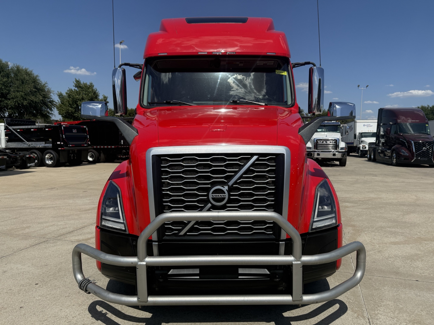 Volvo VNL truck front view with grille guard and bumper, red cab, large grille, wind deflector on the roof.