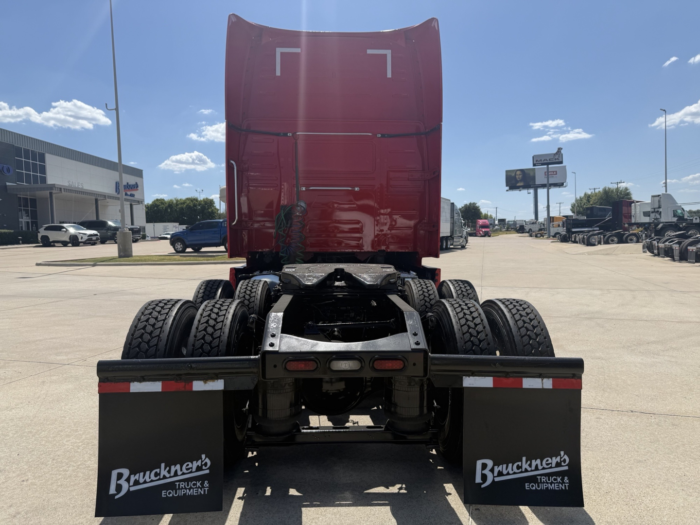 Truck rear view of a 2024 Volvo VNL64T860 sleeper tractor showing chassis and fifth wheel, with red cab high at back and dual rear axles.