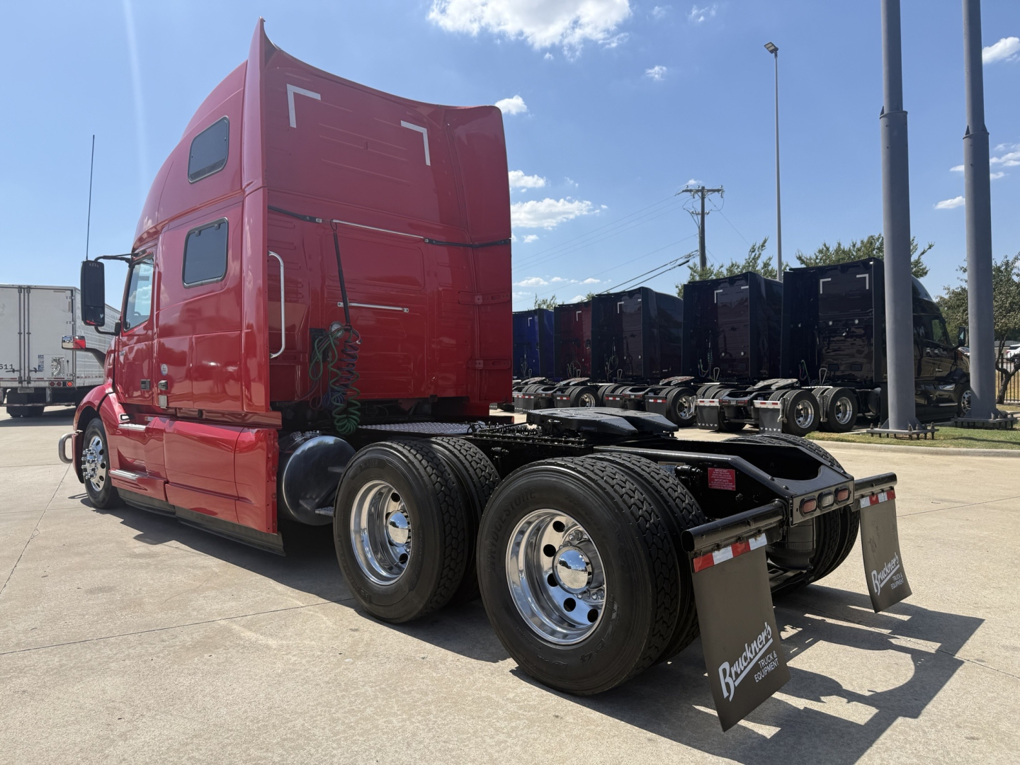 Volvo VNL64T860 truck chassis and sleeper cab side view showing rear wheels and fifth wheel, red cab, black chassis, dealership lot.