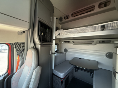 Volvo VNL64T860 sleeper cab interior showing upper bunk, small desk/table, storage compartments, and seating area with light gray upholstery.